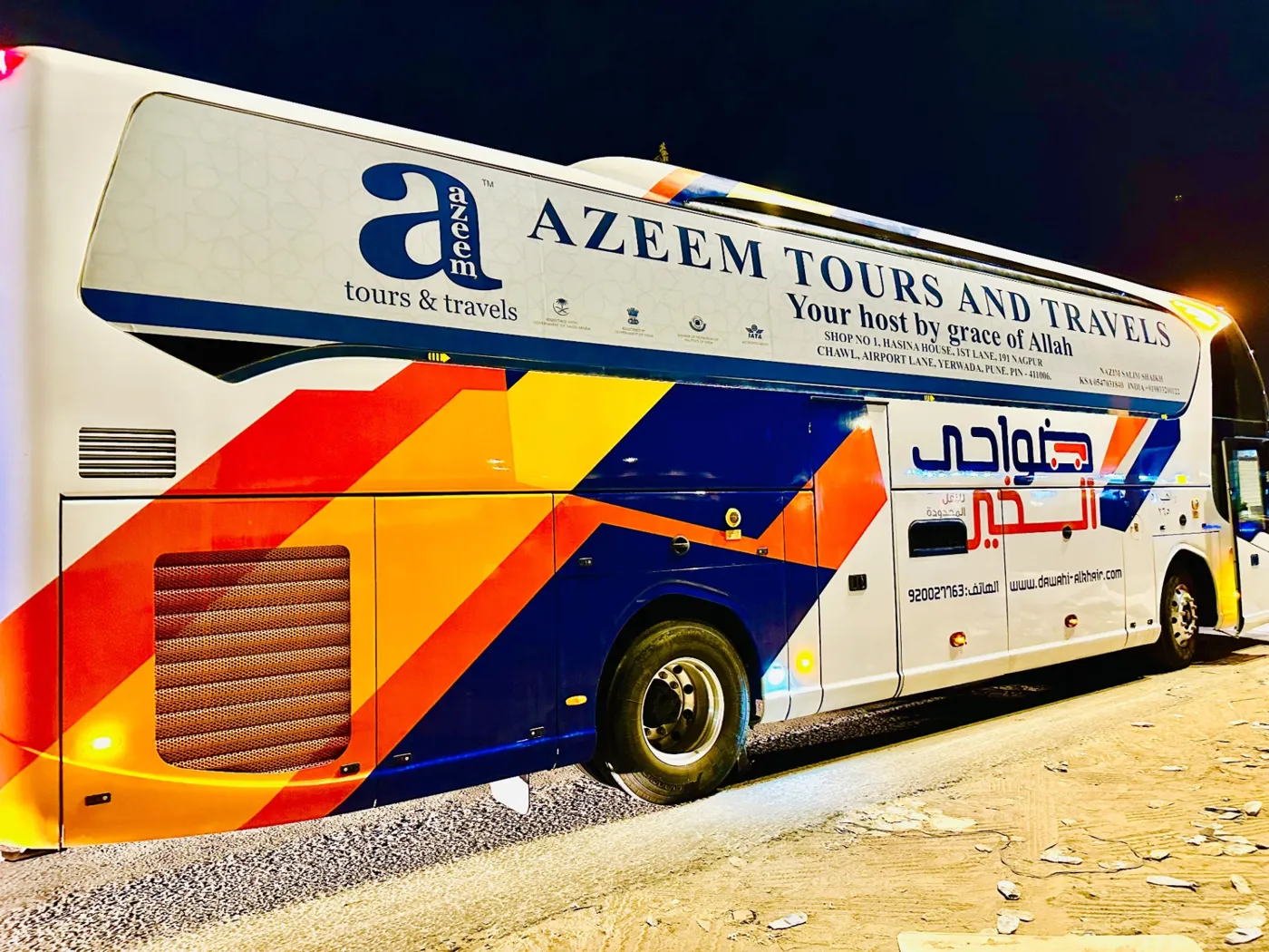 A white Azeem Tours and Travels branded coach parked at night in Saudi Arabia