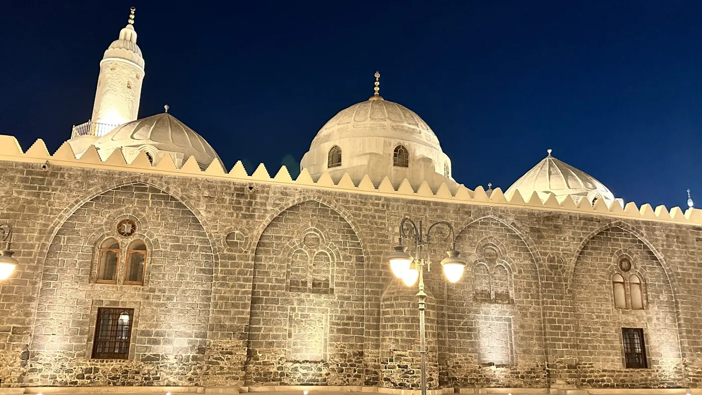 The stone walls and white domes of Masjid Al Ghamama lit up against a deep blue Madinah night sky