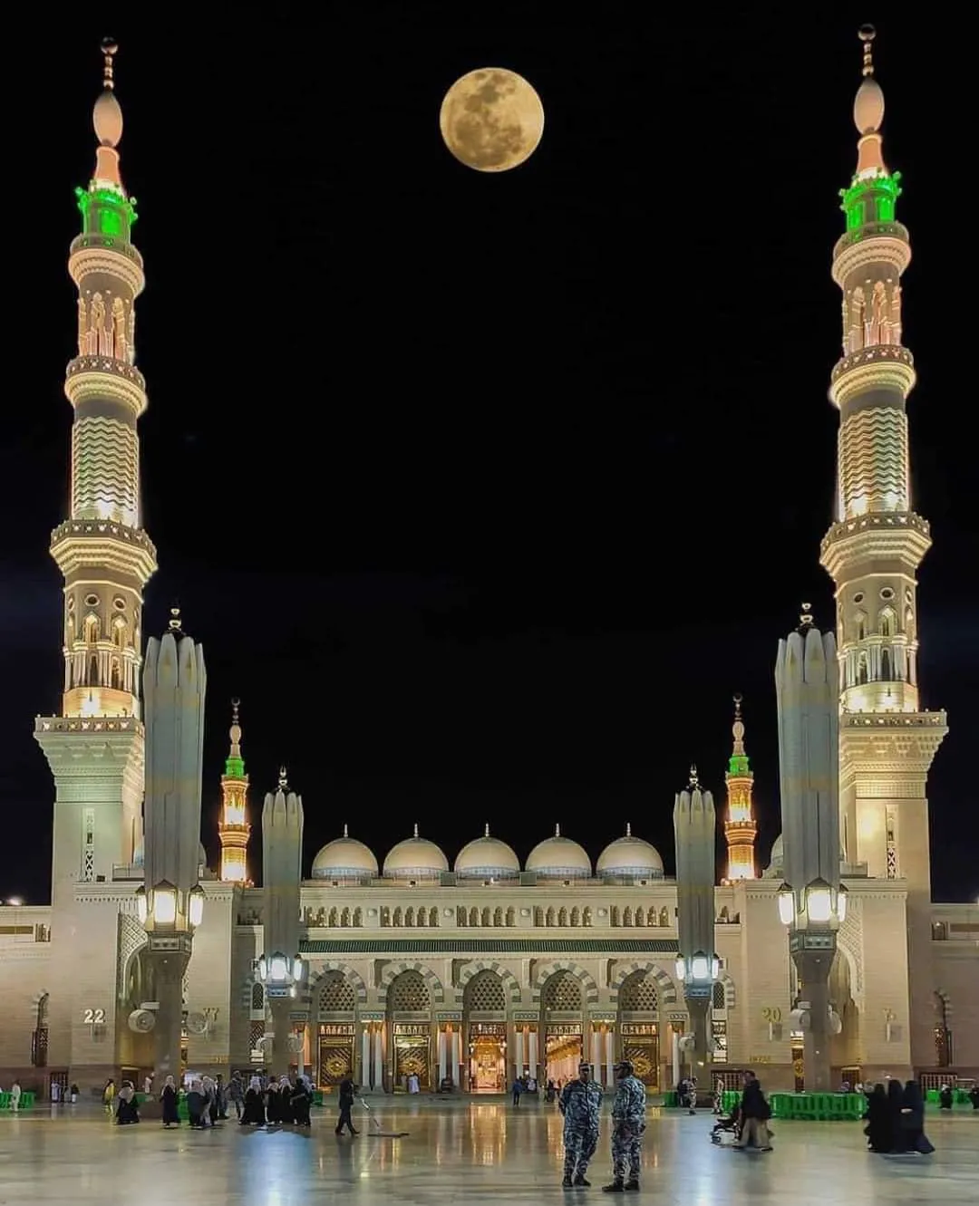 The illuminated minarets and domes of Masjid an-Nabawi at night with a full moon above