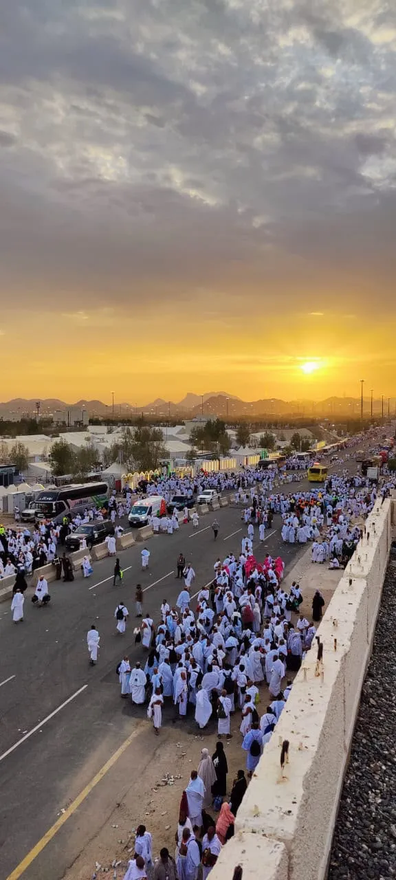 Thousands of pilgrims in white walking along a road at sunrise with mountains on the horizon