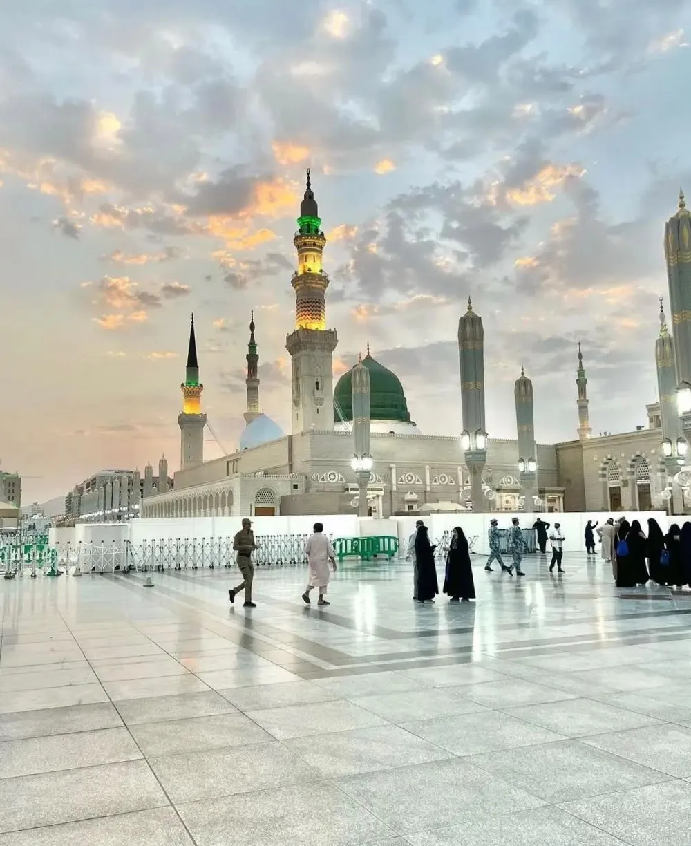 Masjid an-Nabawi with its Green Dome and lit minarets under a pastel sunset sky