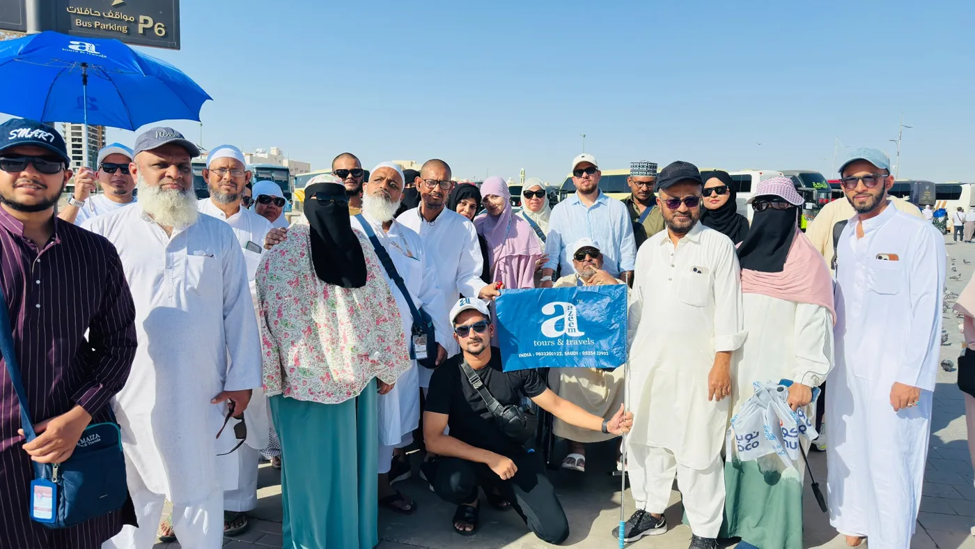 Azeem Tours pilgrims posing together, a guide kneeling in front with the blue Azeem flag